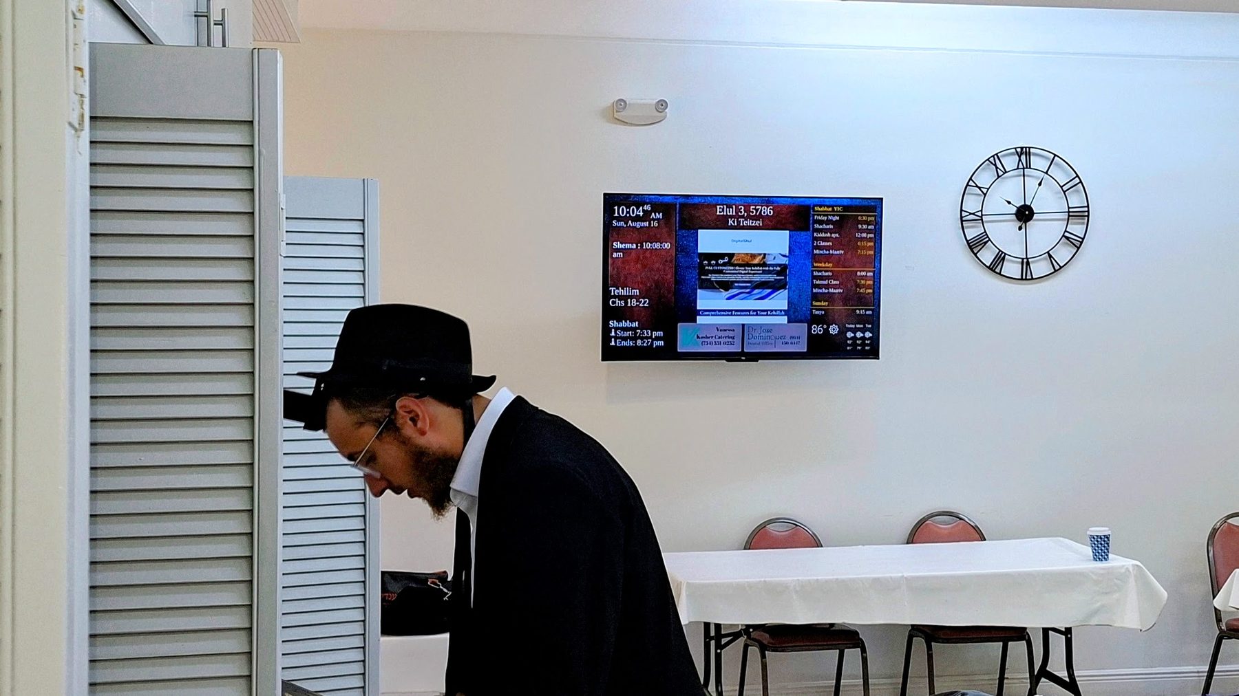 DigitalShul zmanim display installed on the wall of a synagogue in Pembroke Pines, showing halachic prayer times, the Hebrew date, Shabbat schedule and community advertising