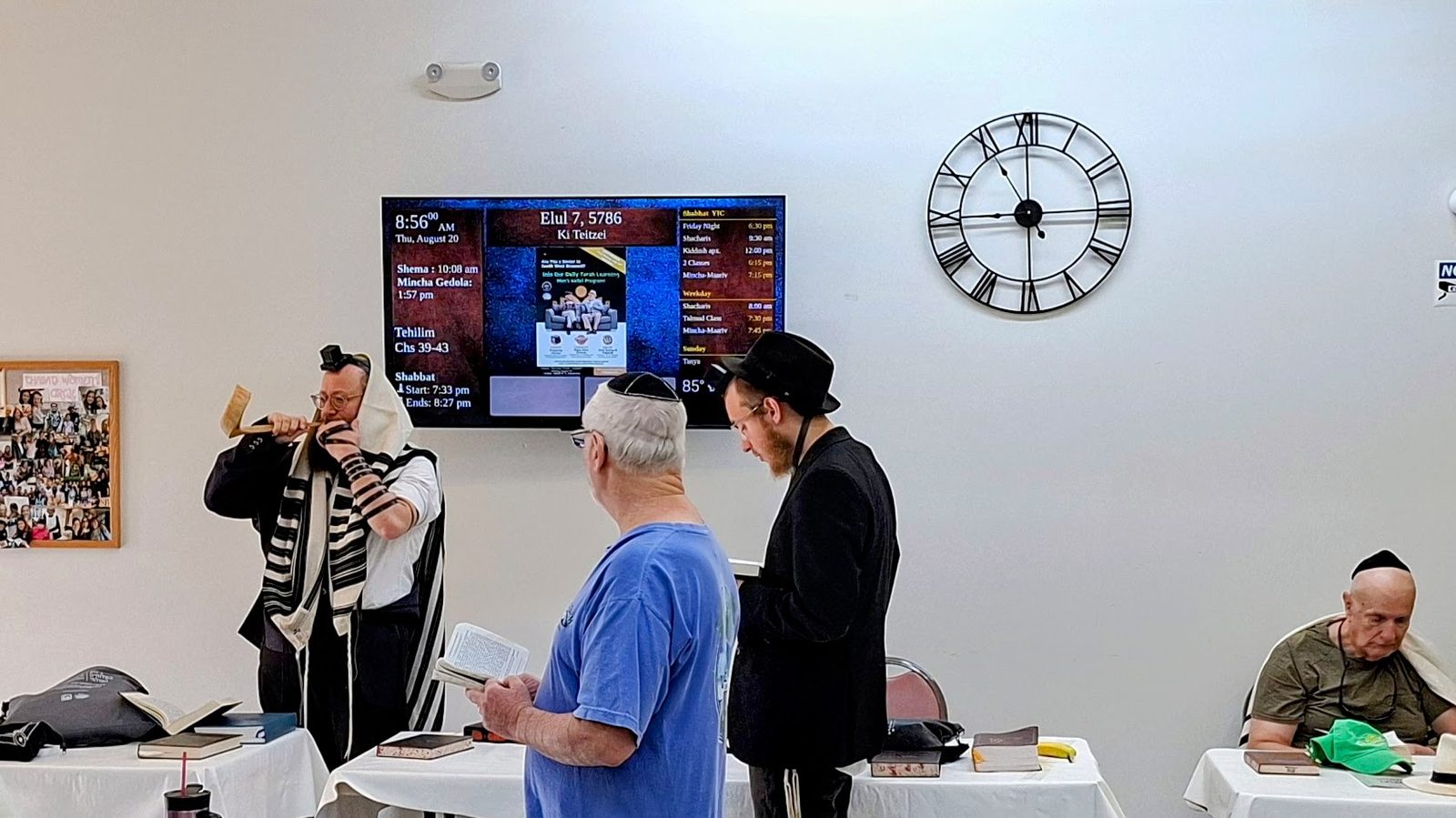 Morning minyan during Elul with the shofar being blown, the DigitalShul screen showing the Hebrew date on the wall